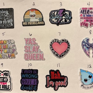 May include: A collection of twelve colorful badge reels with various designs and text. The designs include phrases like "Going back to bed," "No probllama," and "Ask me about my custom badge reels." The badge reels are a mix of shapes and colors.