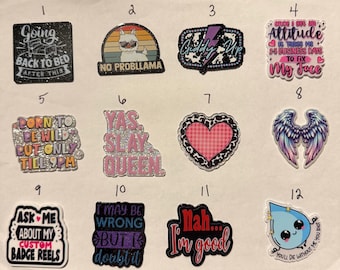 May include: A collection of twelve colorful badge reels with various designs and text. The designs include phrases like "Going back to bed," "No probllama," and "Ask me about my custom badge reels." The badge reels are a mix of shapes and colors.