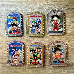 May include: Six rectangular metal Dragon Ball Evolution character cards. Each card features a different colorful illustration of characters from the Dragon Ball anime series. The cards have a glittery border and the Dragon Ball Evolution logo.