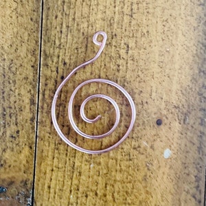 May include: A copper wire spiral pendant with a loop at the top. The spiral is a single continuous piece of wire.