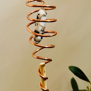 May include: A copper wire spiral with a white and black crystal stone wrapped in gold wire. The spiral is attached to a wooden dowel.