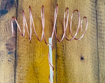 May include: A copper wire sculpture of the word "Millie" on a white background.