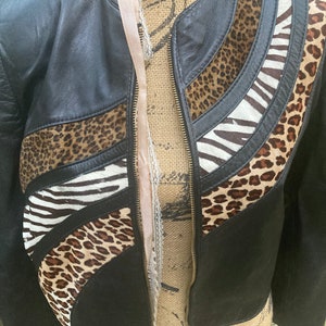 May include: A black leather jacket with a zipper closure. The jacket is decorated with patches of leopard print, zebra print, and brown fur.