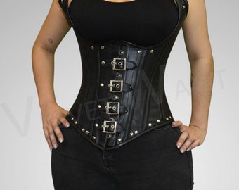 Puede incluir: Un corsé de cuero negro con hebillas y tachuelas plateadas. El corsé tiene un diseño de tirantes halter y se lleva sobre una camiseta sin mangas negra y unos vaqueros negros.