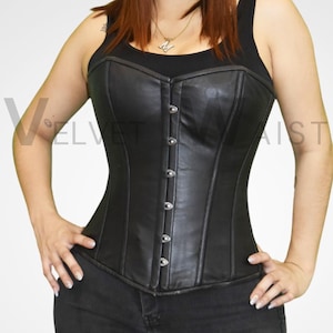 May include: Black leather corset with a scoop neckline and silver-tone metal clasps. The corset has a structured design and is worn over a black tank top and black jeans. The corset is a form-fitting garment.