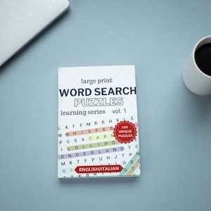 Op de afbeelding: Een wit boek met de titel "Word Search Puzzles" in zwarte tekst. Het boek maakt deel uit van een leerserie en is volume 1. Het boek heeft een rode cirkel met de tekst "100 Unique Puzzles" in witte tekst. Het boek ligt op een lichtblauw oppervlak met een witte koffiemok en een laptop.