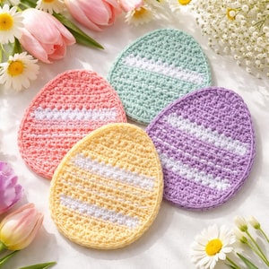 Puede incluir: Cuatro posavasos hechos a mano de ganchillo con forma de huevo en colores pastel: rosa, amarillo, verde y morado. Cada posavasos tiene una franja blanca en el centro. Los posavasos están rodeados de flores, incluyendo tulipanes rosas y margaritas blancas.