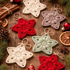 May include: A collection of six star-shaped crochet ornaments in cream, red, sage green, and taupe. Each star features a textured puff stitch center and a simple loop of twine at the top for hanging, arranged on a dark wooden surface.