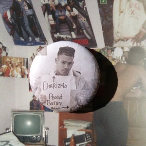 Può includere: Un bottone in bianco e nero con il ritratto di un giovane uomo e il testo "Charizma Peanut Butter Wolf" scritto su di esso.