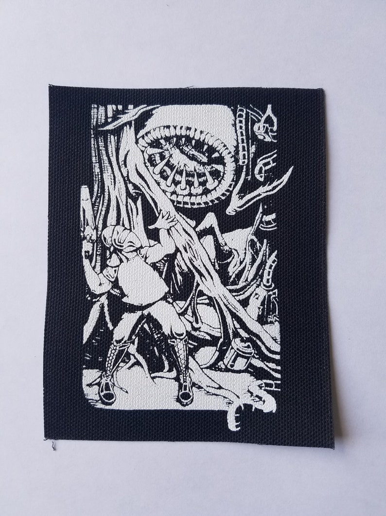 May include: Black and white embroidered patch featuring a person holding a weapon and facing a large, circular, alien-like creature with tentacles.