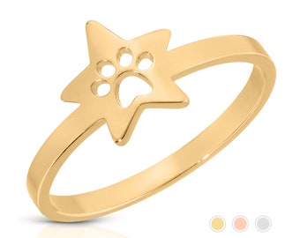 May include: A gold-colored ring featuring a star-shaped design with a paw print cutout. The ring has a smooth, polished finish and a delicate band. The paw print adds a playful touch to the jewelry.