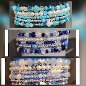 May include: Stackable beaded bracelets in shades of blue, white, and silver. Each bracelet features a variety of beads, including pearls, crystals, and small round beads. Some bracelets have heart and star charms.