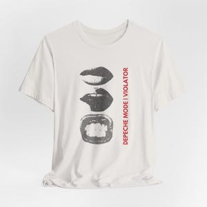 Może przedstawiać: Biała koszulka z grafiką trzech szarych ust ułożonych pionowo. Tekst "DEPECHE MODE | VIOLATOR" jest wydrukowany na czerwono po prawej stronie. Koszulka ma krótkie rękawy i okrągły dekolt.