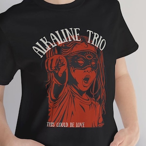 May include: Black t-shirt with a red and white illustration of a masked girl pointing with the text "Alkaline Trio" and "This Could Be Love" printed on the front.