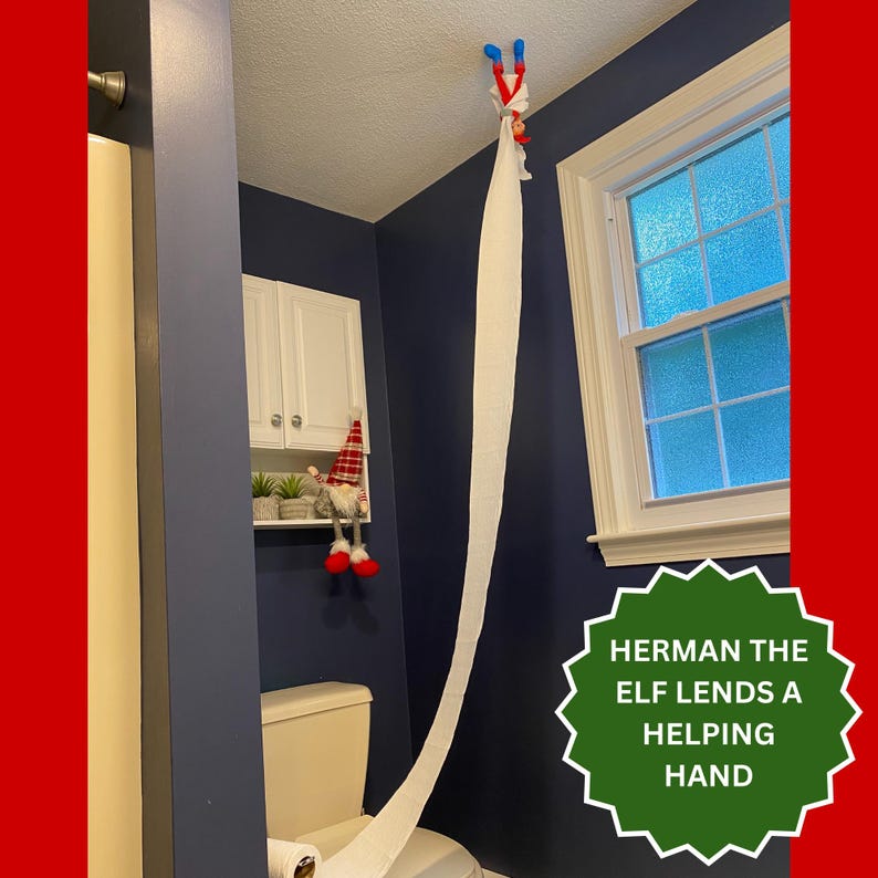 May include: A small elf doll with a red and white hat hanging from the ceiling by a long strip of white toilet paper that extends down to the toilet. A second gnome-like doll with a red plaid hat sits on a white shelf above the toilet.