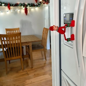 A Christmas Elf climbing up a refrigerator wearing his Enchanted Elf Boots.