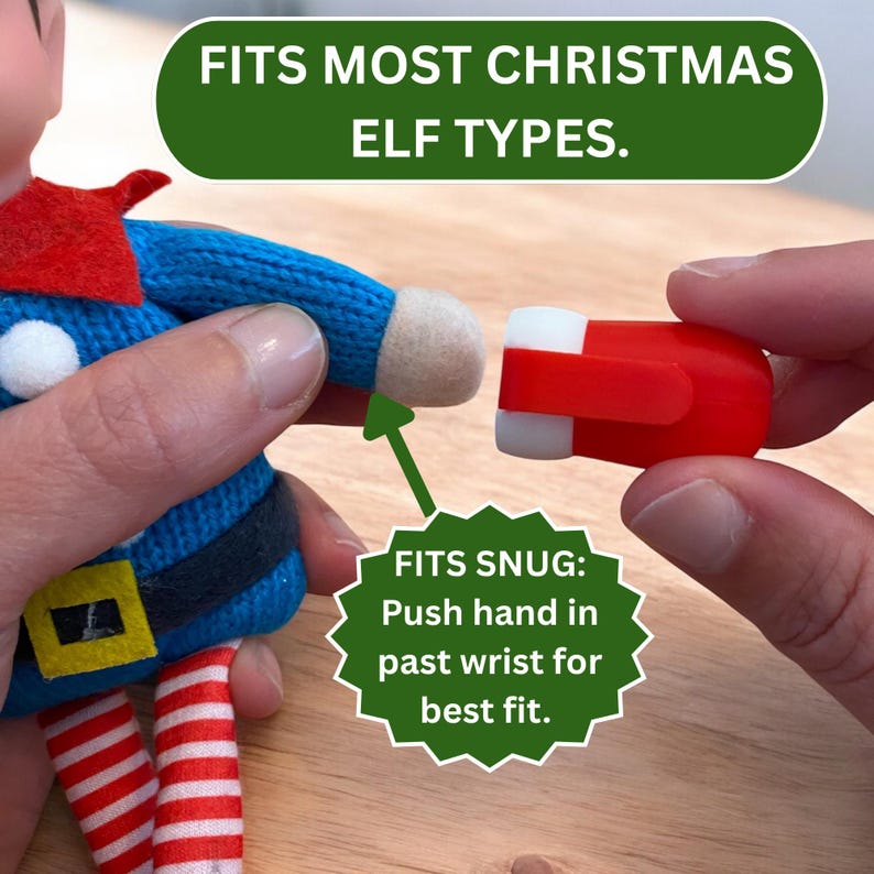 May include: A small red plastic accessory with white ends, designed to fit onto the hand of a blue knitted elf doll. The image includes text stating FITS MOST CHRISTMAS ELF TYPES and FITS SNUG: Push hand in past wrist for best fit.