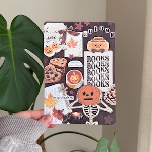 May include: A collage-style print featuring autumn-themed elements. Includes images of pumpkins, cookies, a cinnamon roll, and the word "autumn". Text includes "BOOKS" and "in my kindle era". The color palette is warm, with browns, oranges, and reds.