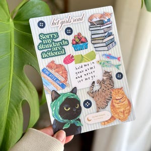 May include: A decorative sticker sheet featuring cat illustrations and text. The sheet includes images of cats, books, and phrases like "hot girls read" and "Sorry, my standards are fictional." The design incorporates blue, green, and orange accents.