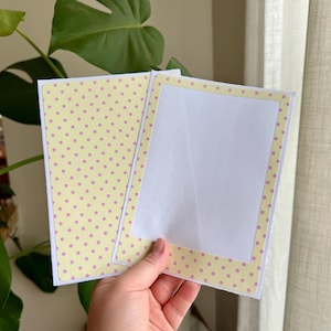 May include: A rectangular greeting card with a light yellow background featuring a pattern of small pink polka dots. The card is open, revealing a plain white interior panel framed by a matching yellow and pink polka dot border on the right side.