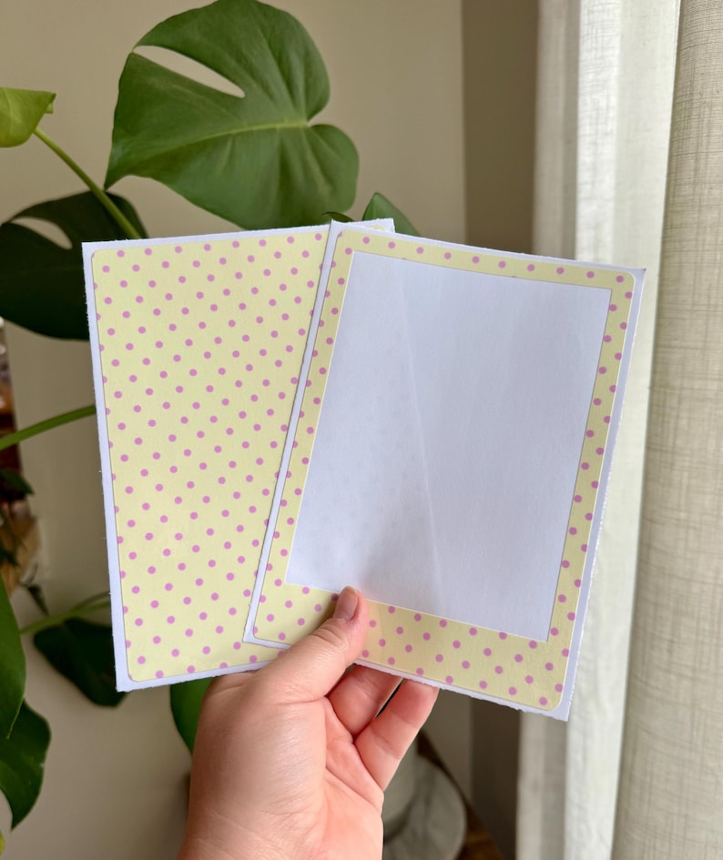 May include: A rectangular greeting card with a light yellow background featuring a pattern of small pink polka dots. The card is open, revealing a plain white interior panel framed by a matching yellow and pink polka dot border on the right side.