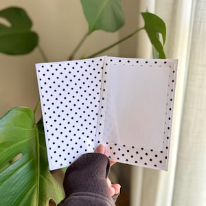 May include: A rectangular greeting card featuring a black and white polka dot pattern on the exterior and interior panels. The card includes a central white rectangular frame on the right side, designed for a photo or message, with rounded corners.