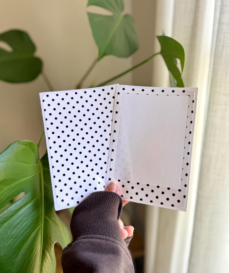 May include: A rectangular greeting card featuring a black and white polka dot pattern on the exterior and interior panels. The card includes a central white rectangular frame on the right side, designed for a photo or message, with rounded corners.