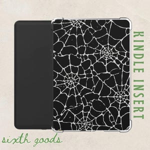 Könnte beinhalten: Schwarzer Kindle-Einsatz mit weißem Spinnennetz-Design. Der Einsatz befindet sich neben einem schwarzen Kindle. Die Worte "Kindle Insert" sind vertikal in Grün gedruckt. Die Worte "sixth goods" sind in Grün gedruckt.