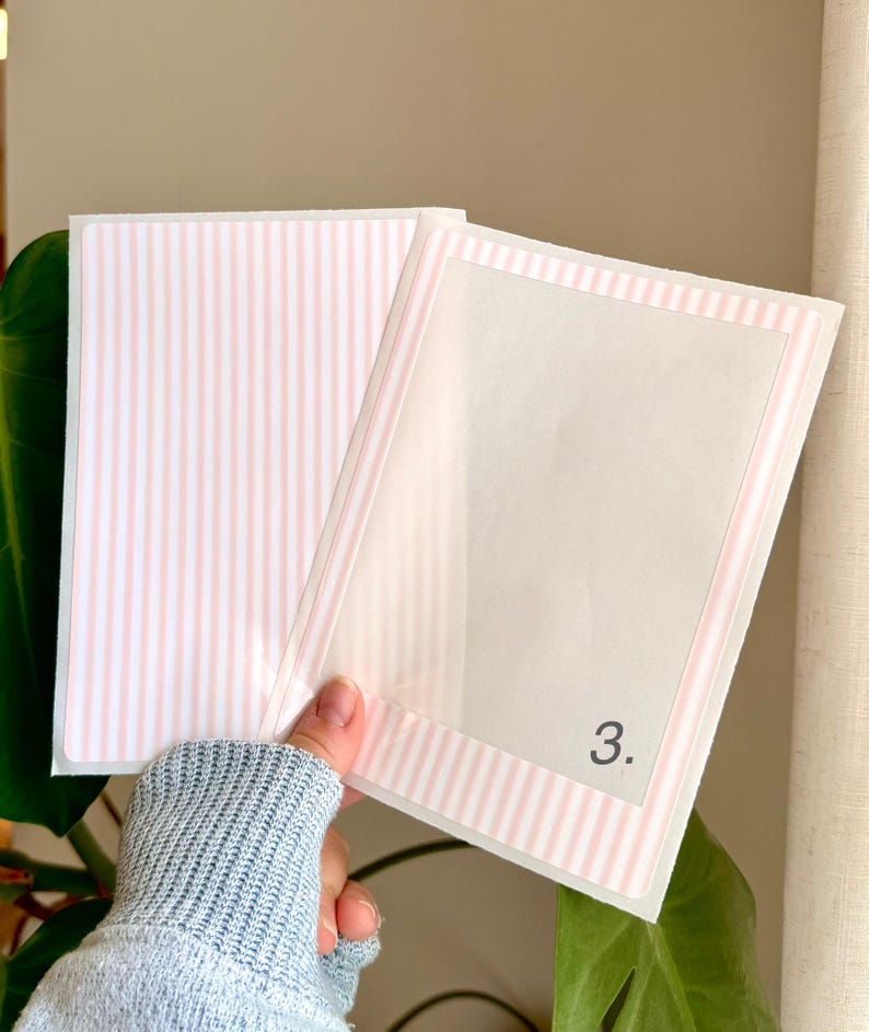May include: A clear plastic sleeve with a pink and white striped border and interior. The number "3." is printed in black on the front. The sleeve is open, revealing a pink and white striped interior.