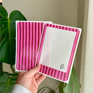 May include: Two white cards with pink and burgundy striped borders and accents. One card has a blank white space, the other has a vertical striped pattern. The number "6." is printed on the blank card.