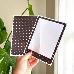 May include: Two rectangular cards with a dark brown background featuring a white polka dot pattern. One card is fully covered in the pattern, while the other card has a wide dark brown border with white polka dots surrounding a plain white centre.