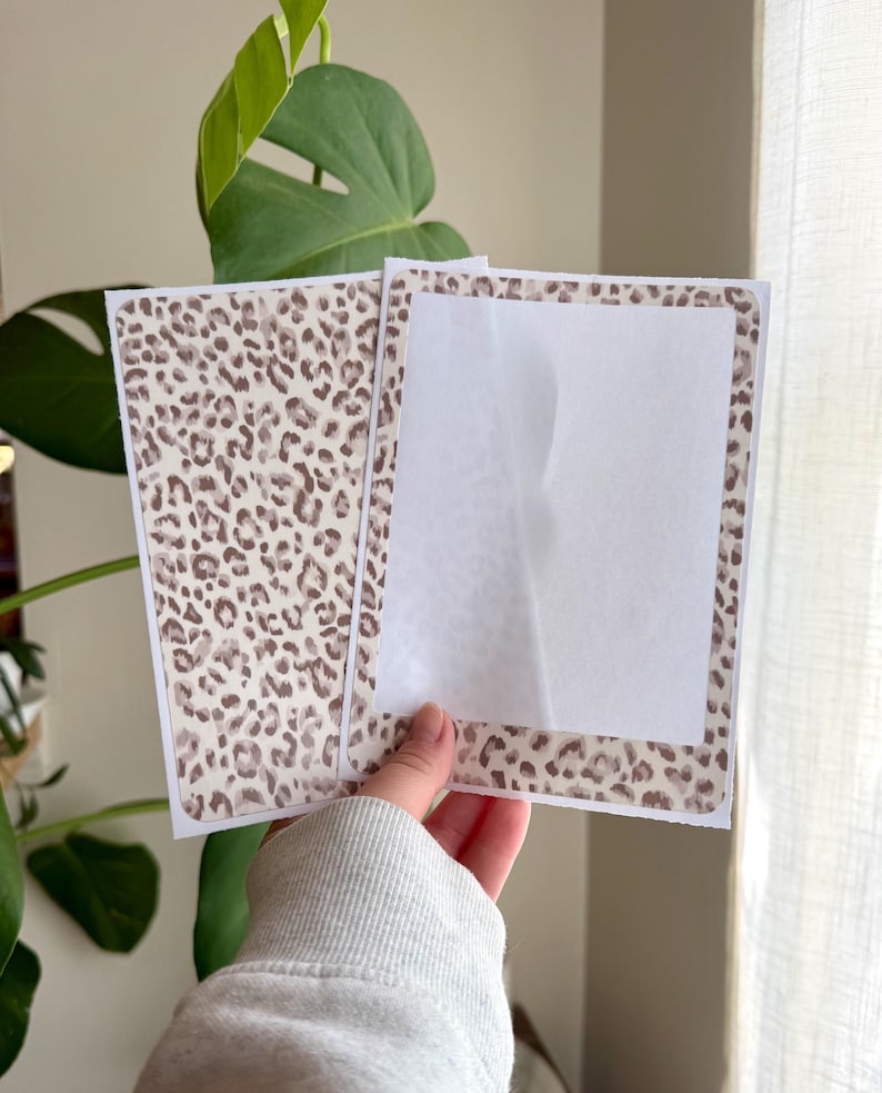 May include: Two rectangular paper cards featuring a brown and beige leopard print pattern. One card displays the full animal print design, while the other card features a leopard print border surrounding a large, blank, white rectangular center area.