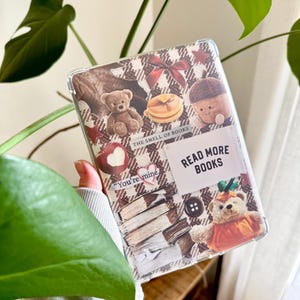 Op de afbeelding: Transparante telefoonhoes met een collage-ontwerp met teddyberen, pannenkoeken en boeken. De hoes heeft de tekst "READ MORE BOOKS" en "THE SMELL OF BOOKS".