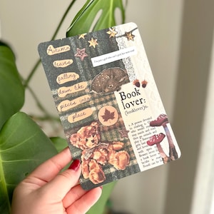 May include: A rectangular card featuring a dark green plaid background with collage elements including a brown teddy bear, a fawn, red mushrooms, and star accents. Text includes "Autumn leaves falling down like pieces into place" and a definition of "Book lover".