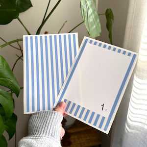 May include: Two rectangular cards with a light blue and white vertical stripe pattern. One card is fully striped, while the other features a white centre panel framed by the striped border and includes the black printed number 1 in the corner.