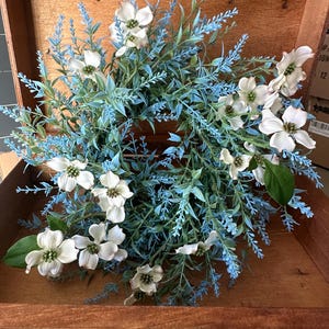 May include: A blue and white floral wreath with white dogwood blossoms and blue foliage. The wreath is in a wooden box with a leather handle.