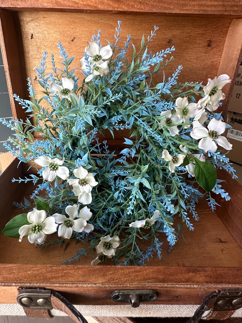 May include: A blue and white floral wreath with white dogwood blossoms and blue foliage. The wreath is in a wooden box with a leather handle.