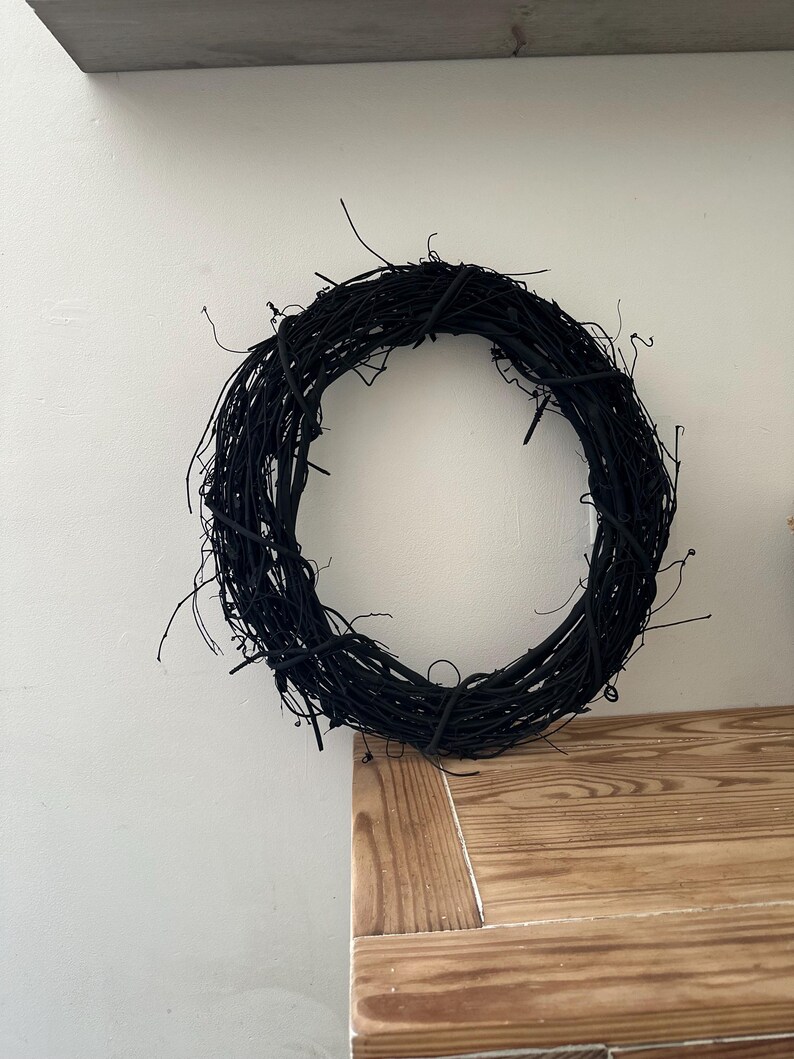May include: A circular wreath constructed from thin, intertwined twigs and branches, entirely painted in a matte black finish. The structure features a dense, organic arrangement of woody stems with numerous small, protruding ends.