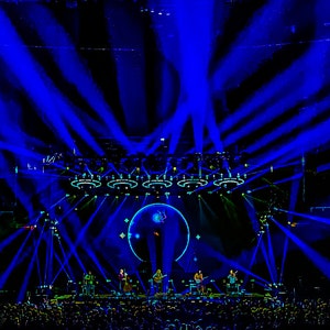 Peut inclure: Scène de concert éclairée de lumière bleue. Un groupe se produit devant un public nombreux. Des faisceaux de lumière bleue vive rayonnent du haut de la scène, créant un effet visuel dynamique. L'arrière-plan comprend un motif circulaire.