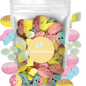 Puede incluir: Una bolsa de plástico transparente llena de caramelos de goma de colores. Los caramelos incluyen formas de calaveras, formas ovaladas con la palabra "Bubs" y otras formas variadas en amarillo, rosa, azul y verde. Un círculo amarillo con el texto "USA Swedish Candy" está en el centro.
