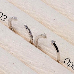 May include: Three open silver rings with small gemstones are displayed on a cream-coloured fabric. The rings are labelled "Open Ring 02" and "Open Ring 01". The brand name "AMELIA MINIMALIST moissanite jewelry" is at the bottom.