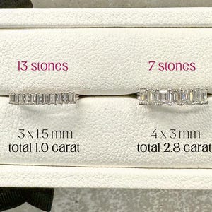 May include: Two half eternity rings with emerald cut stones are displayed in a white box. One ring has 13 stones, measuring 3 x 1.5 mm, totaling 1.0 carat. The other has 7 stones, measuring 4 x 3 mm, totaling 2.8 carats. The text reads "EMERALD CUT half eternity."