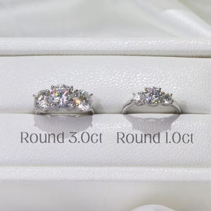 May include: Two silver rings with round-cut stones are displayed in a white box. The larger ring is labeled "Round 3.0ct" and the smaller ring is labeled "Round 1.0ct". The brand name "AMELIA MINIMALIST moissanite jewelry" is printed at the bottom.