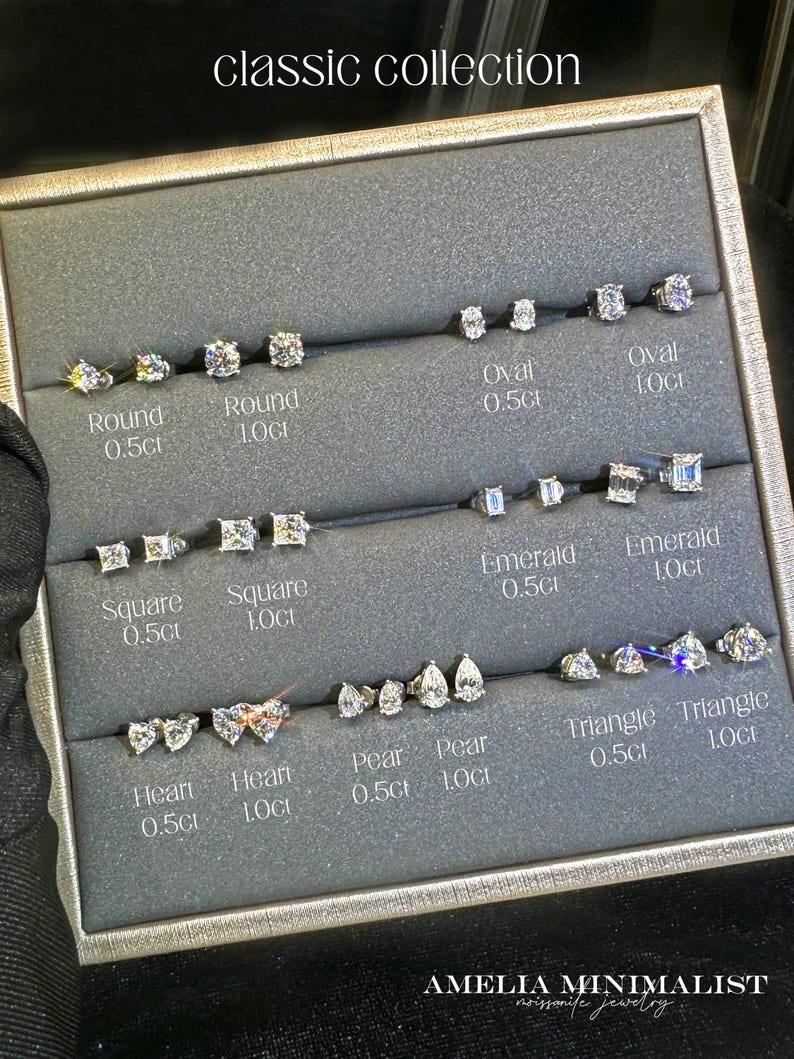 Puede incluir: Un expositor con la etiqueta classic collection que contiene pares de pendientes de bot&oacute;n en varias formas, incluyendo redonda, ovalada, esmeralda, cuadrada, coraz&oacute;n, pera y tri&aacute;ngulo, etiquetados con pesos de 0,5ct o 1,0ct por Amelia Minimalist.