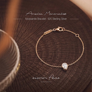 May include: A gold-toned chain bracelet featuring a single pear-shaped moissanite stone. The bracelet includes a lobster clasp and a small rectangular tag stamped with 925. Text on the image reads Amelia Minimalist Moissanite Bracelet 925 Sterling Silver 4x6mm Pear.