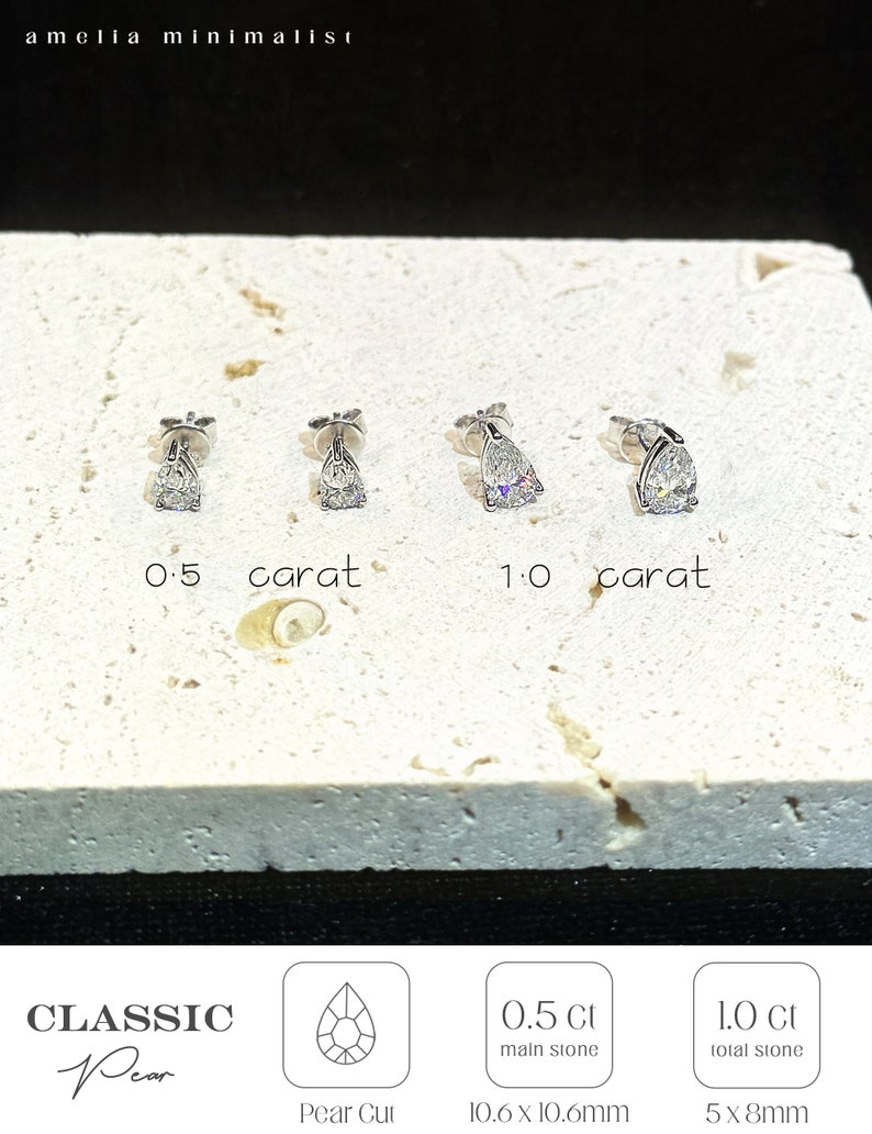 Puede incluir: Cuatro pendientes de bot&oacute;n plateados con corte de pera, dispuestos en dos pares. El primer par est&aacute; etiquetado como 0,5 quilates y el segundo como 1,0 quilates. El texto incluye amelia minimalist, CLASSIC Pear, Pear Cut, 0,5 Ct main stone y 1,0 Ct total stone.