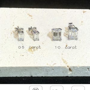 Puede incluir: Cuatro pendientes de bot&oacute;n plateados con piedras de corte esmeralda. Dos pendientes est&aacute;n etiquetados como 0,5 quilates y dos como 1,0 quilates. El texto incluye amelia minimalist, CLASSIC Emerald, Emerald Cut, 0,5 Ct each weight 3x5mm y 1,0 Ct each weight 5x7mm.
