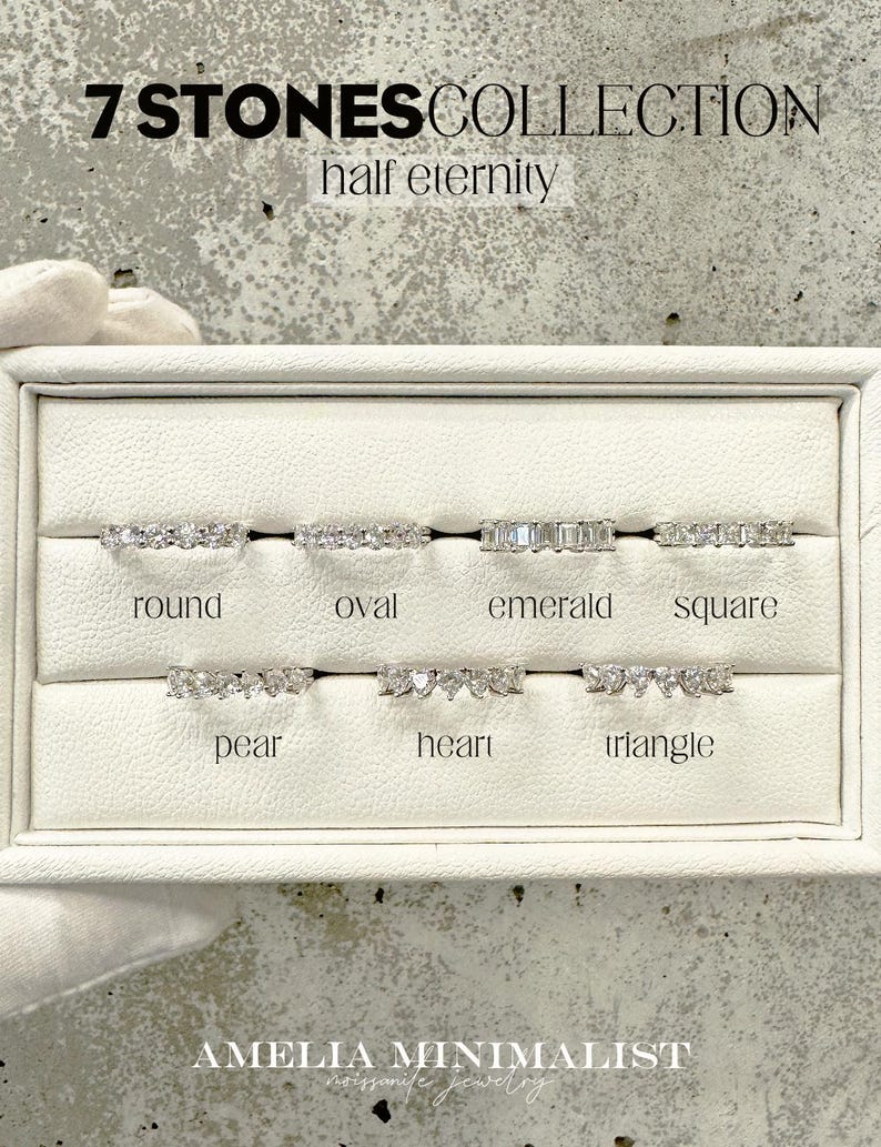 K&ouml;nnte beinhalten: Eine wei&szlig;e Pr&auml;sentationsbox mit sieben verschiedenen Stilen von Halb-Eternity-Ringen, die mit klaren Steinen besetzt sind. Die Ringe sind mit "rund", "oval", "Smaragd", "quadratisch", "Birne", "Herz" und "Dreieck" beschriftet. Der Text "7 STONES COLLECTION half eternity" befindet sich oben im Bild.