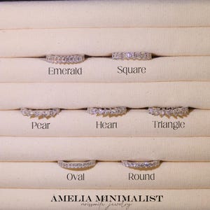 May include: A display of silver rings with various gemstone cuts: emerald, square, pear, heart, triangle, oval, and round. The rings are set against a neutral background, with the brand name "AMELIA MINIMALIST" at the bottom.