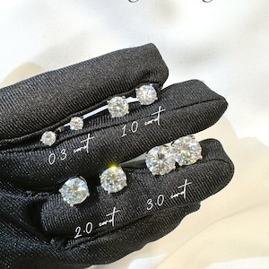 May include: A collection of round-cut stud earrings featuring a 4 prong setting. The image displays pairs labeled with carat weights: 0.3 carat, 1.0 carat, 2.0 carat, and 3.0 carat. Each pair of clear, faceted stones is arranged to show size variations.